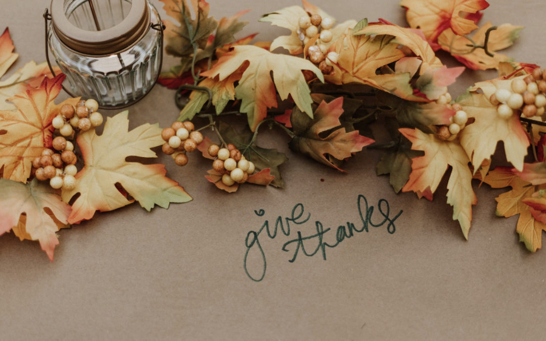 Fall leaves and candle at Thanksgiving place setting that says Give Thanks in scripted writing
