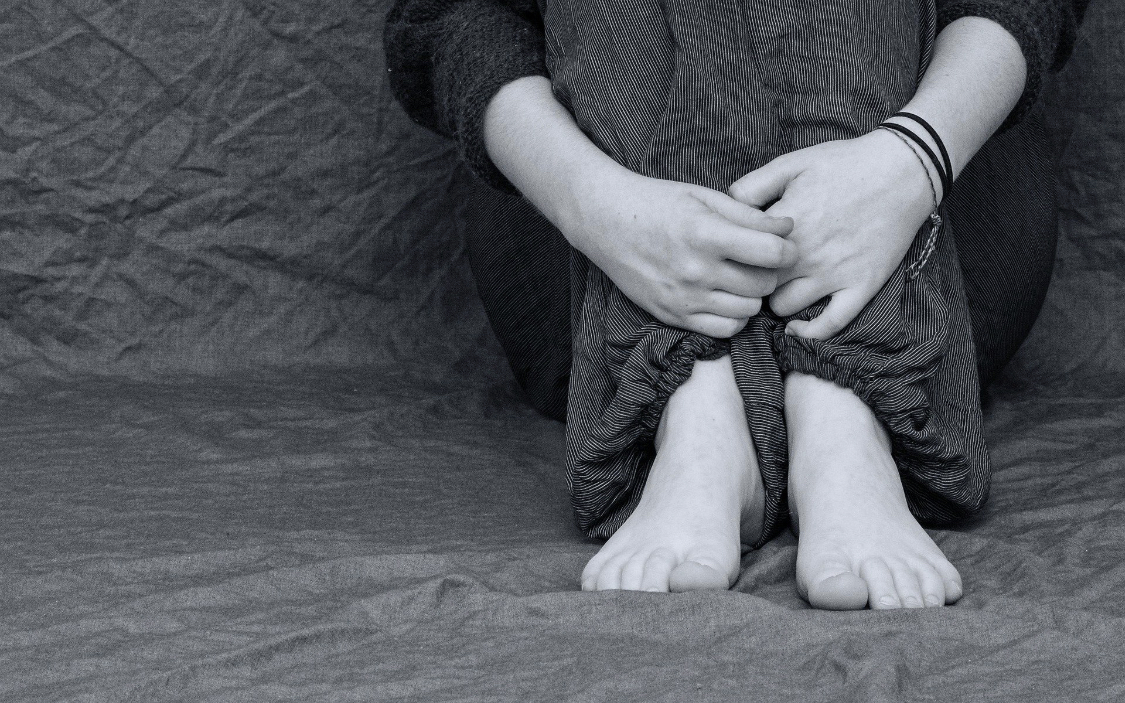 person sits on ground hugging legs. Photo is cropped at knees.