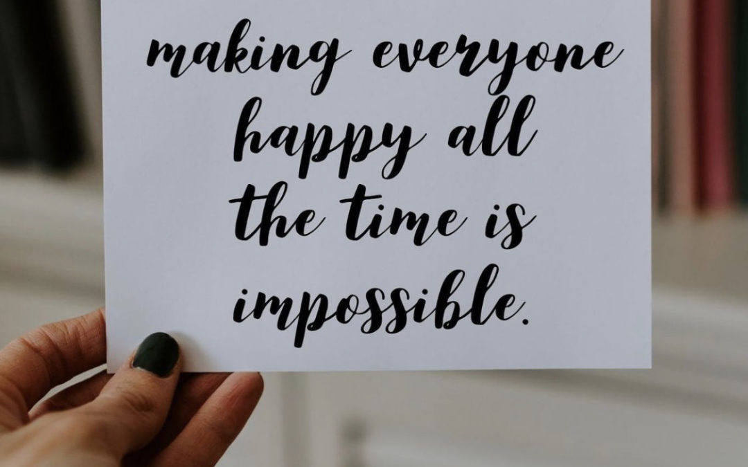 person holding card that says Making everyone happy all the time is impossible